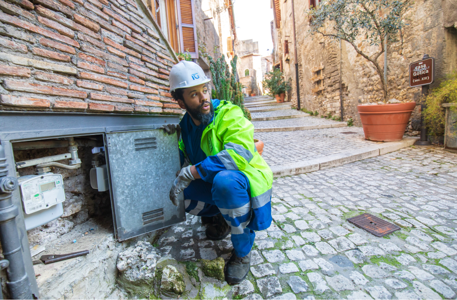 Un operaio Italgas inginocchiato chiude lo sportello di una nicchia murata in una strada di ciottoli, dopo aver installato un contatore Nimbus.