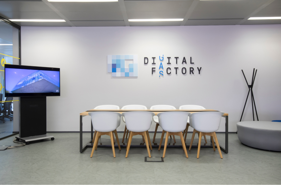 Una sala moderna Digital Factory di Italgas, con tavolo, sedie bianche e monitor, promuove l'innovazione e l'efficienza.