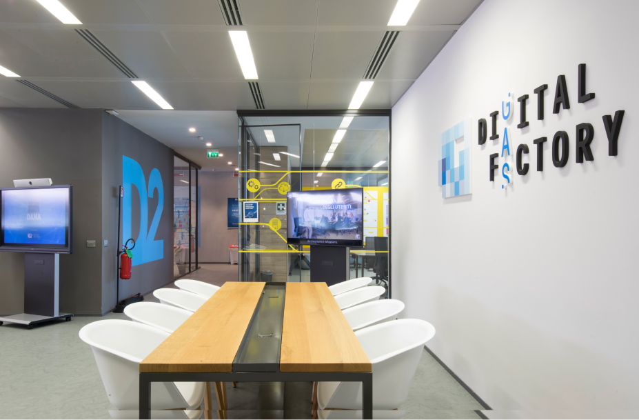 Ufficio moderno Italgas con tavolo riunioni, schermi e parete "DIGITAL FACTORY" che riflette innovazione digitale.