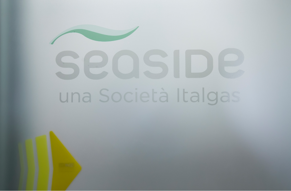 Logo Seaside con onda verde, testo "una Società Italgas" e angolo carta gialla.
