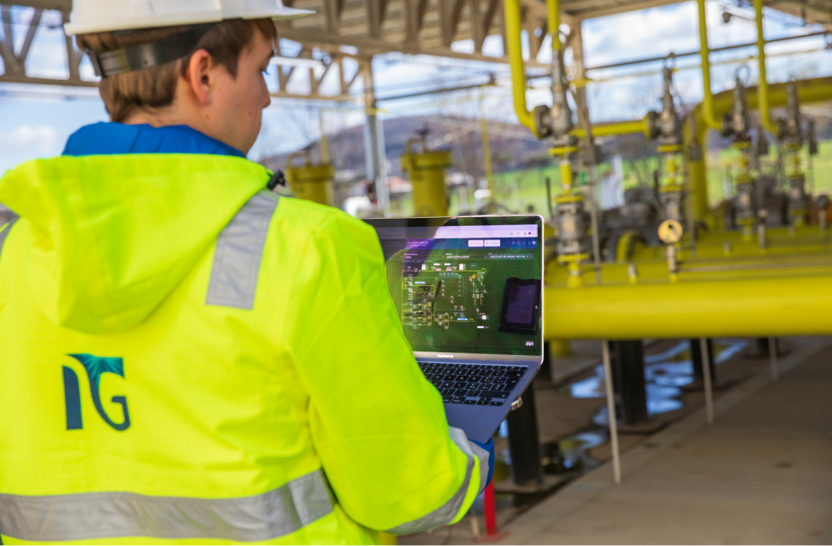 Un tecnico Italgas monitora la rete di biometano con un portatile, in una centrale gas con tubature gialle.
