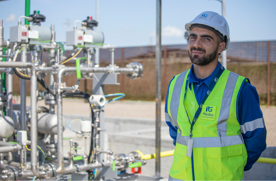 Lavoratore Italgas con caschetto davanti impianto gas, rappresenta l'espansione del metano in Sardegna.