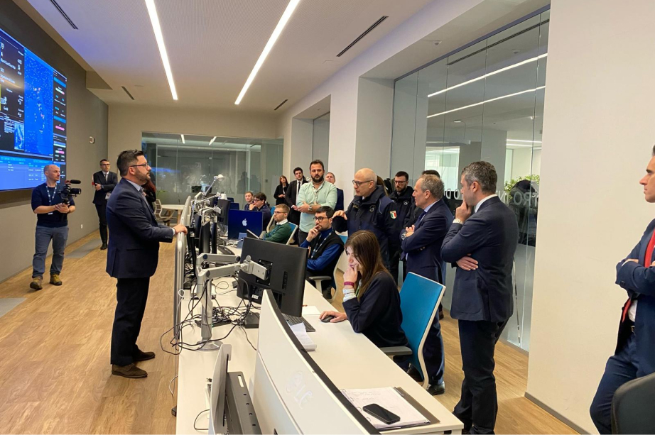 Group of professionals in a control room with monitors at Italgas, discussing work.