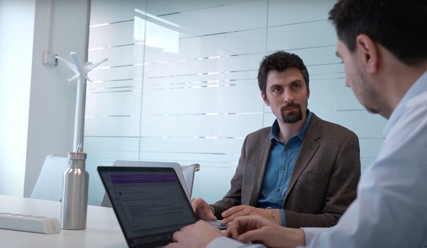 Specialista in innovazione di Italgas in ufficio, conversa con un collega davanti a un laptop. Ambiente moderno.