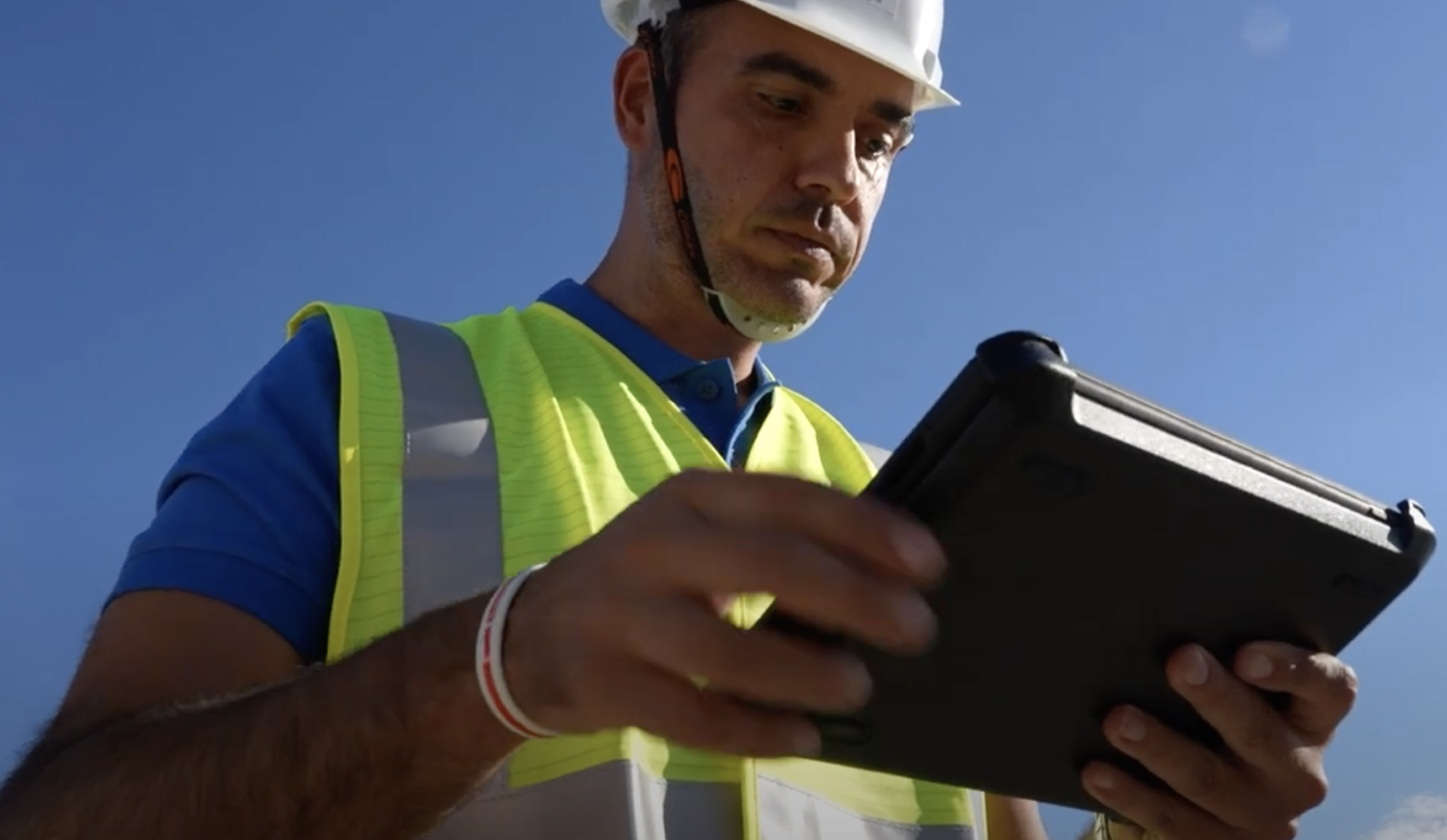 Operatore Italgas in caschetto e giubbotto catarifrangente usa tablet all'aperto.