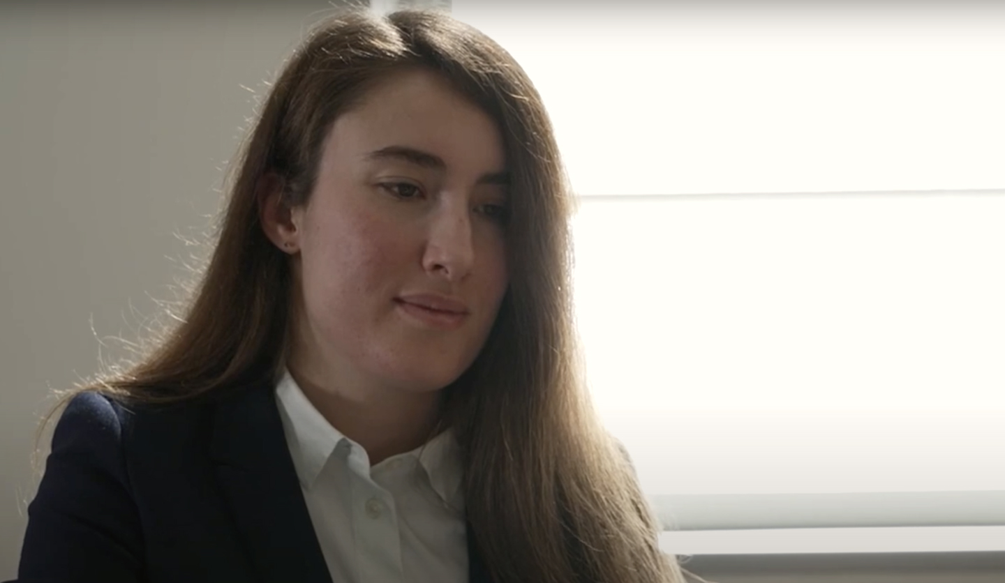 Donna in ufficio con giacca e camicia bianca, sembra concentrata, con luce naturale in sfondo.