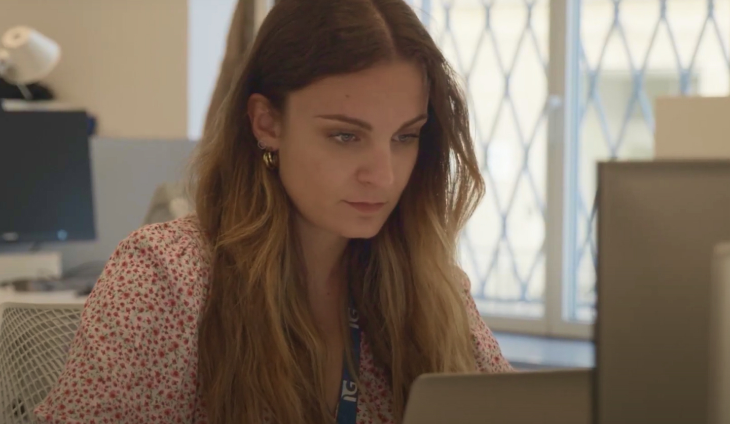 Donna concentrata al lavoro su laptop in ufficio Italgas, indossa badge aziendale.