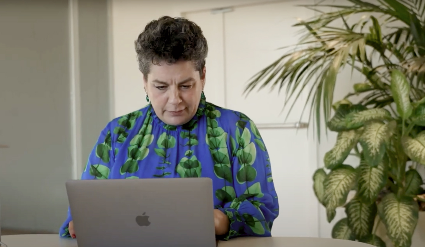 Donna concentrata lavora al computer portatile in ufficio, vestita con una blusa blu e verde.