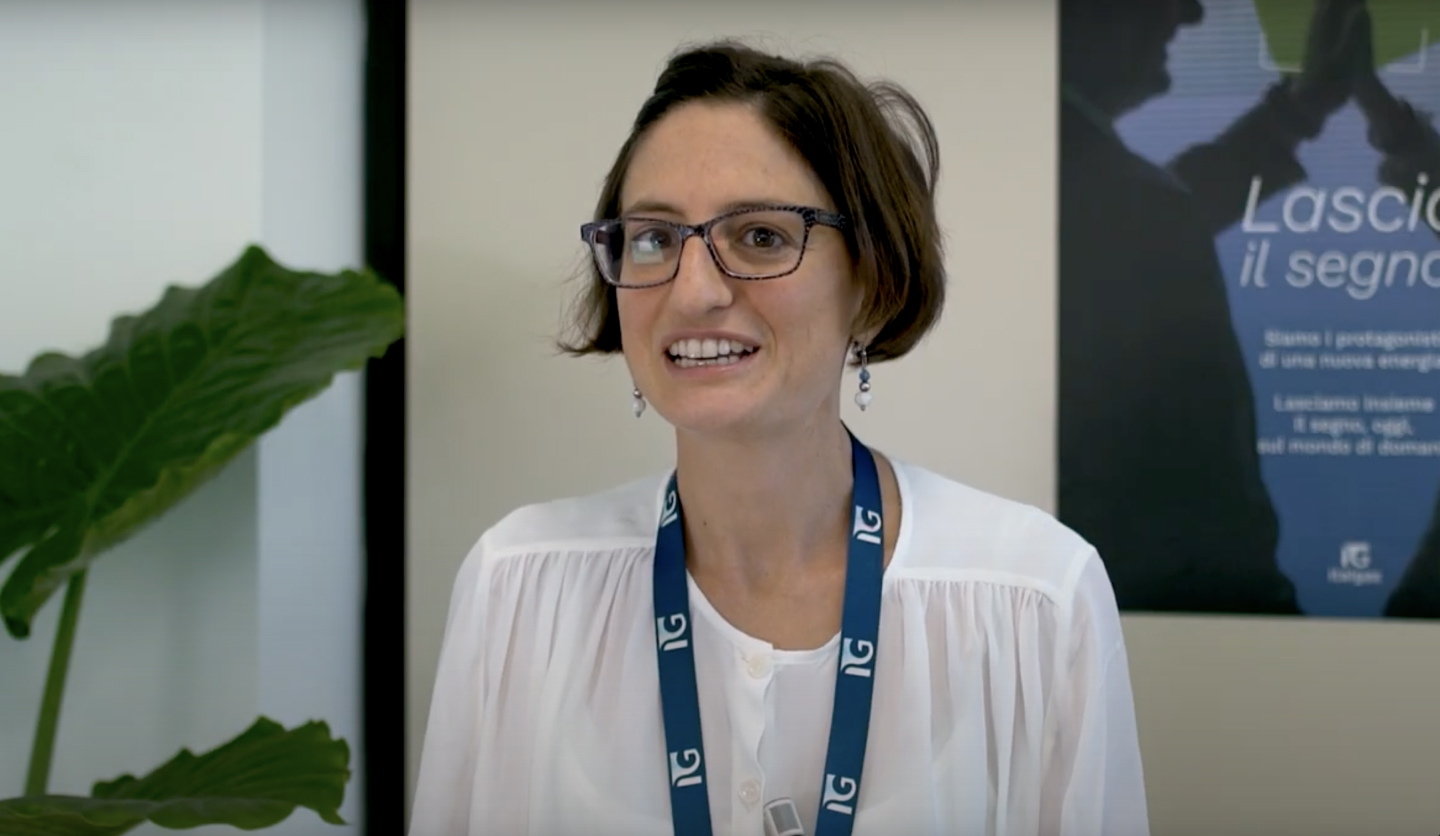 Gestore energia Italgas: donna sorridente con badge, in ufficio, accanto a pianta e poster.