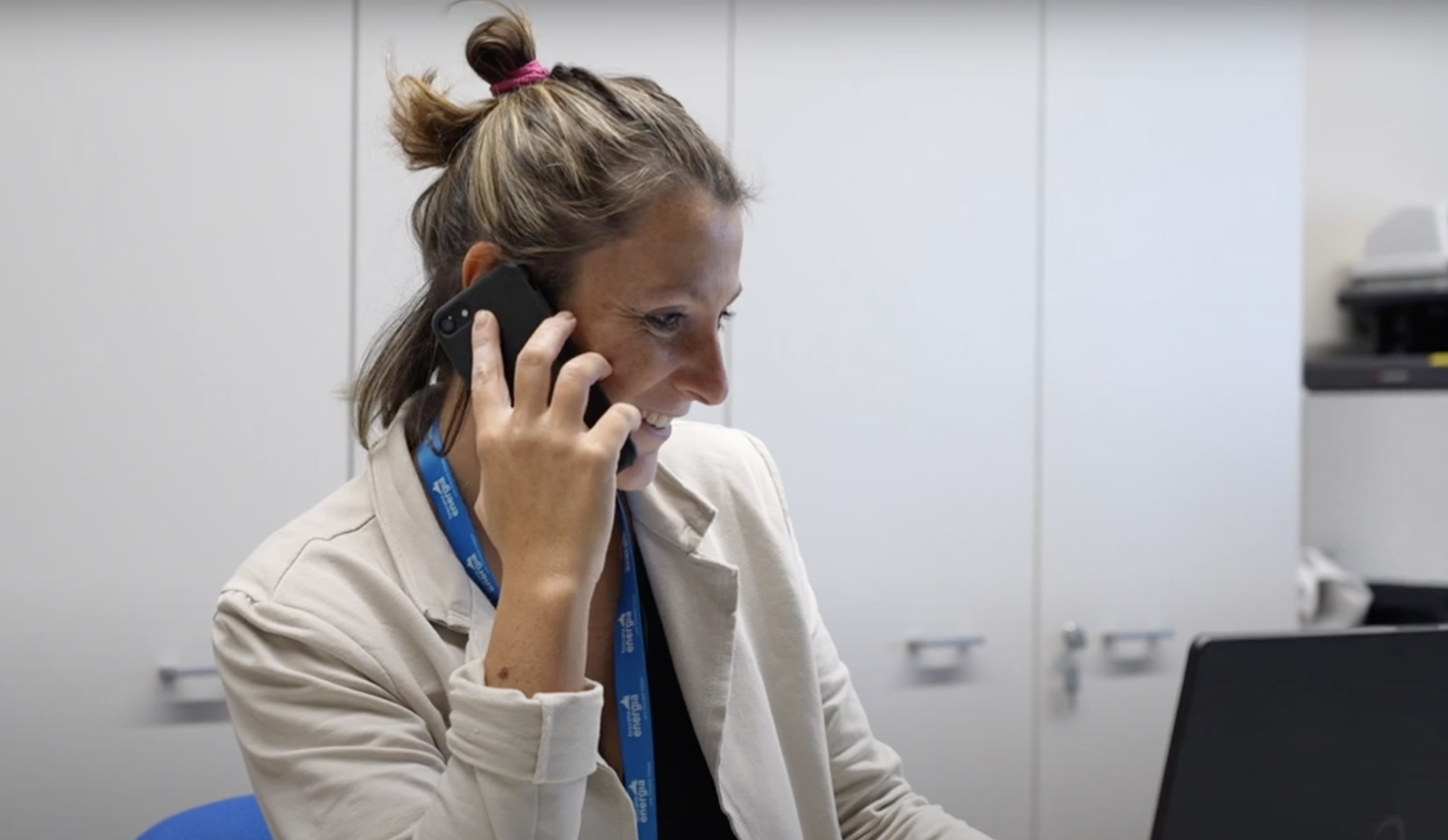 Donna impiegata Italgas parla al telefono e usa il computer in ufficio.