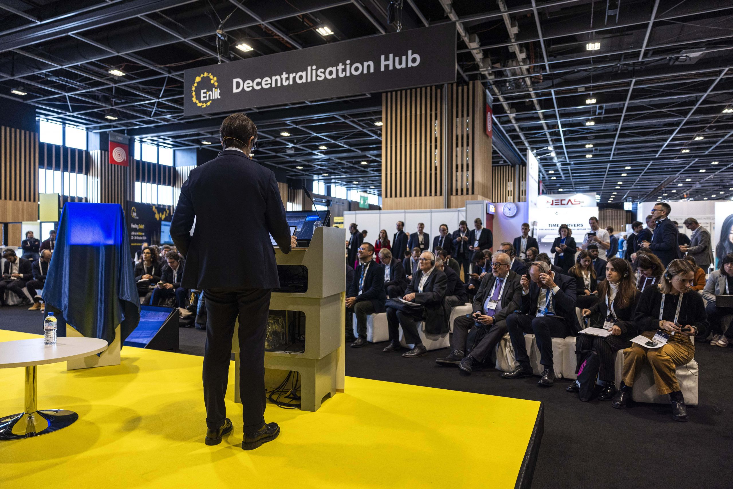 Un relatore presenta al "Decentralisation Hub" di un evento Enlit. Il pubblico, seduto e attento, è composto da professionisti e partecipanti.