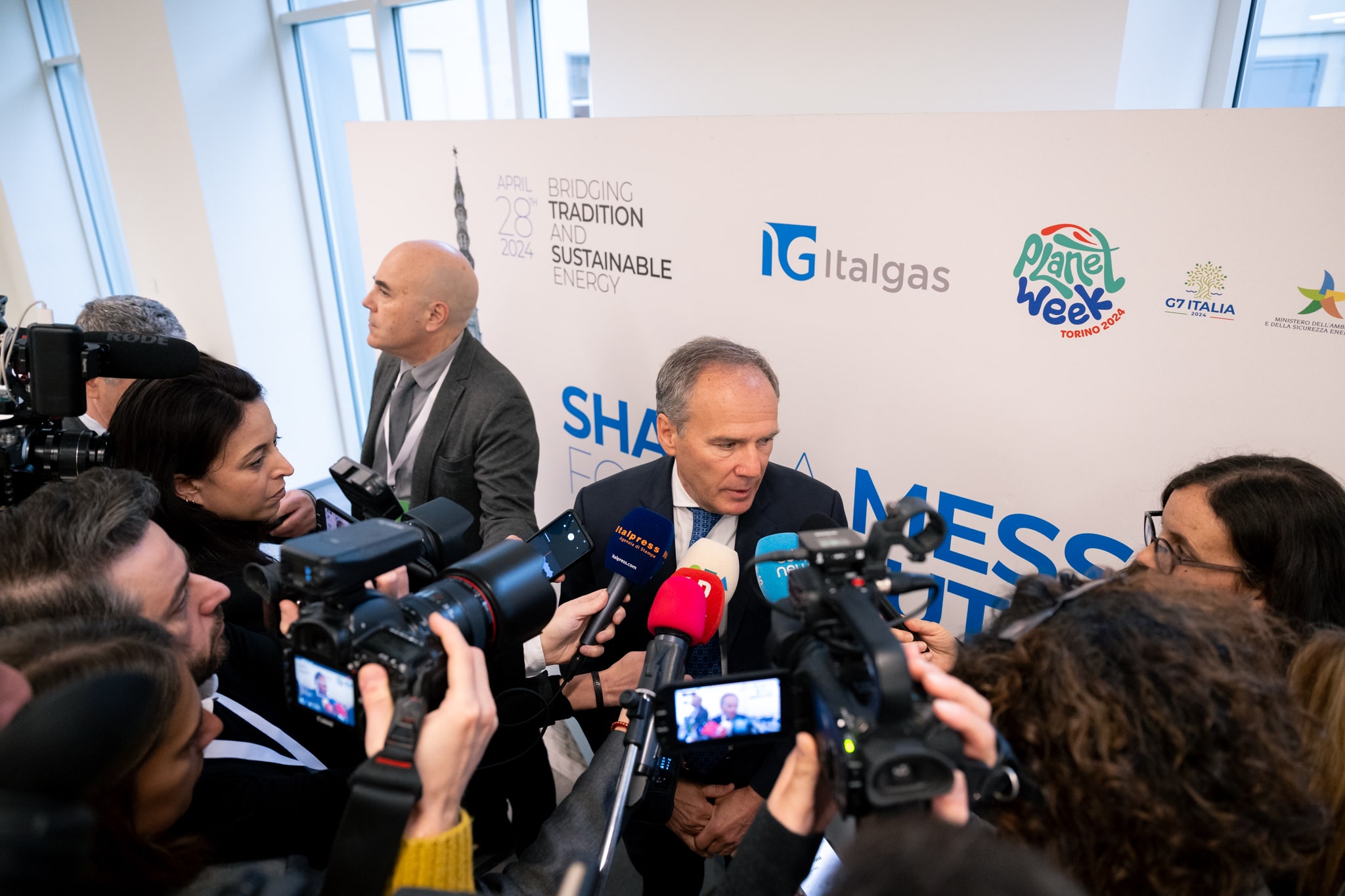 Uomo intervistato da giornalisti alla Planet Week Event di Italgas, con loghi sullo sfondo.
