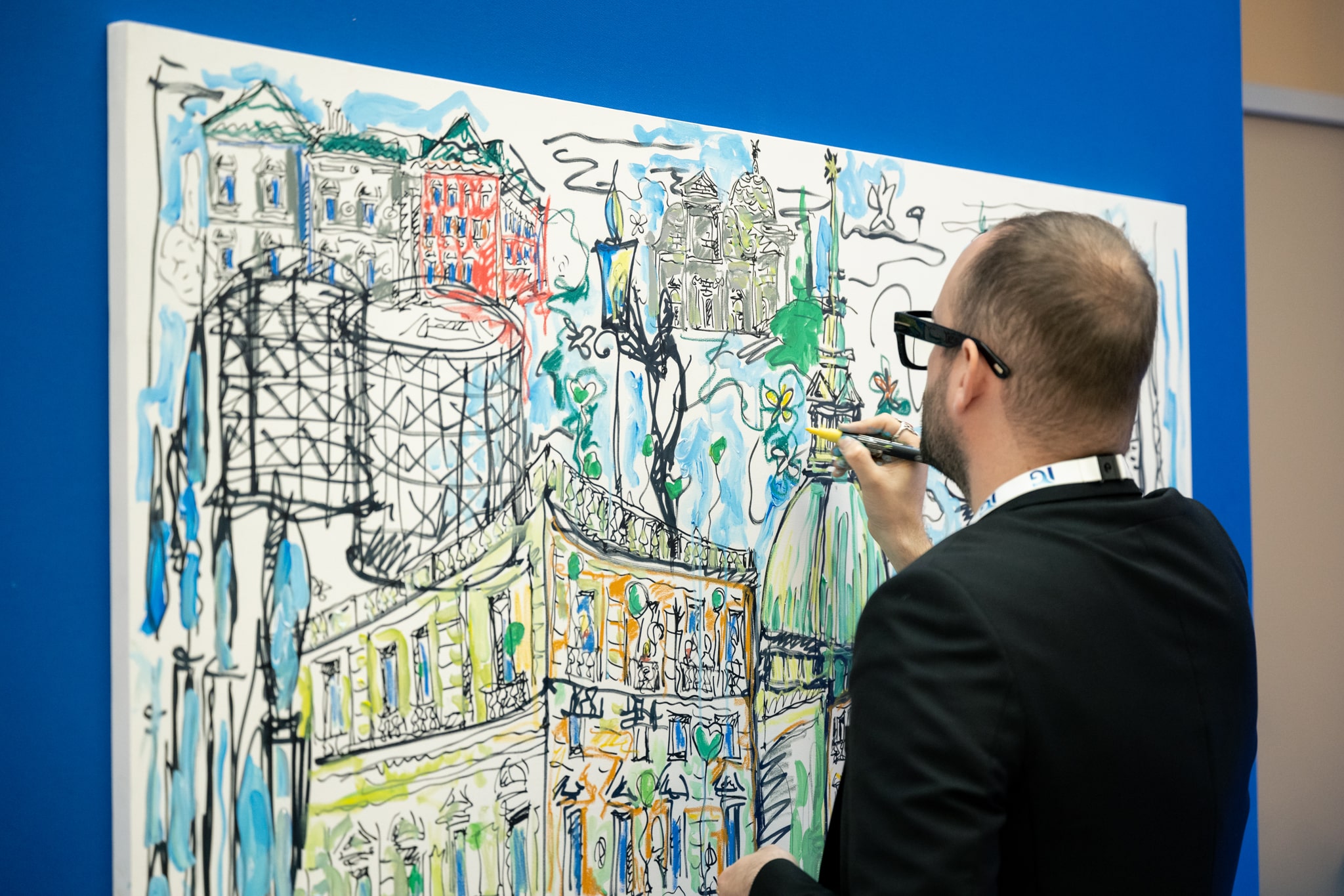 Persona dipinge murale colorato per l'evento Planet Week di Italgas, su sfondo blu.