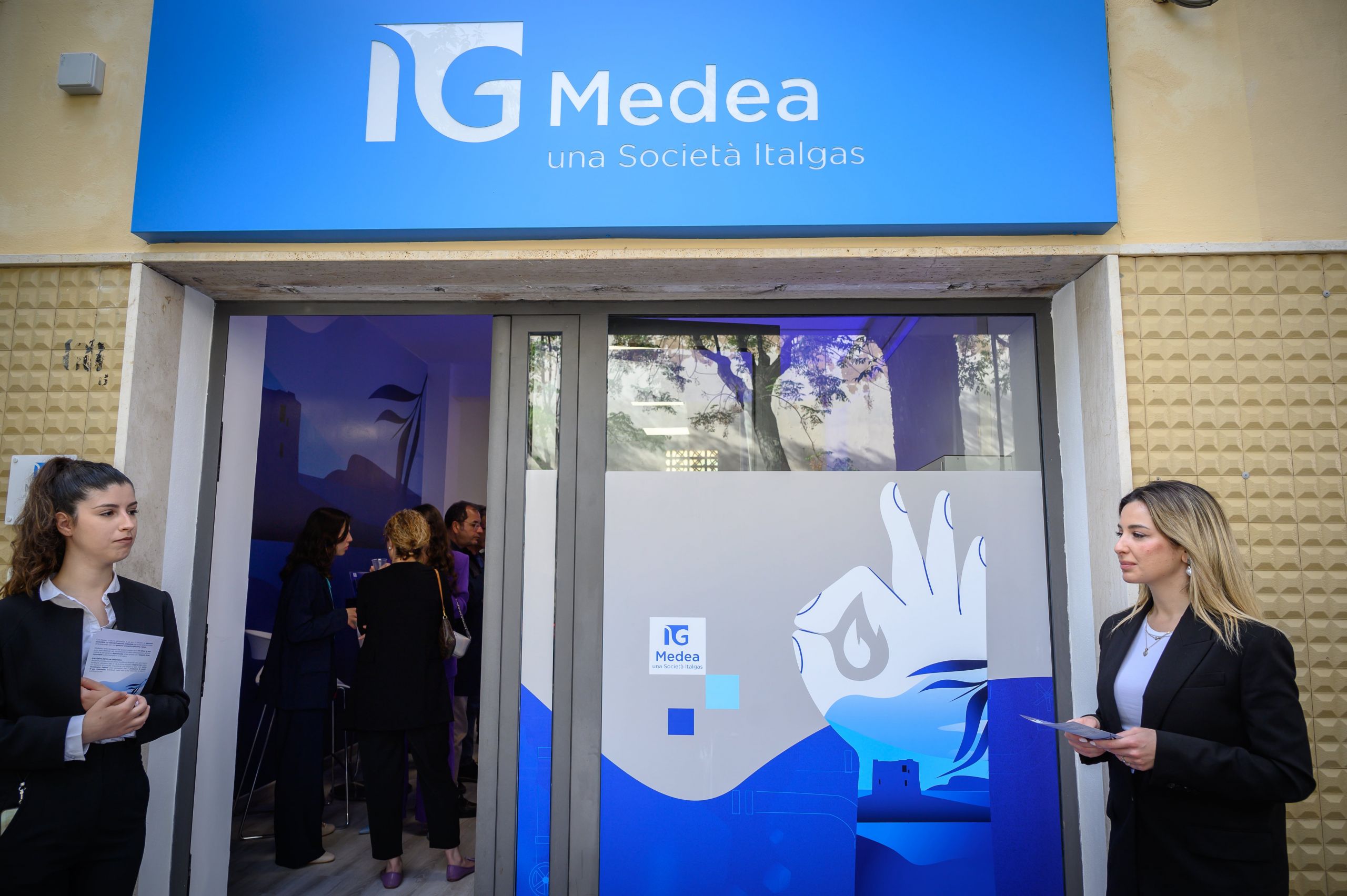Ingresso infopoint Medea Italgas con persone e decorazioni blu.