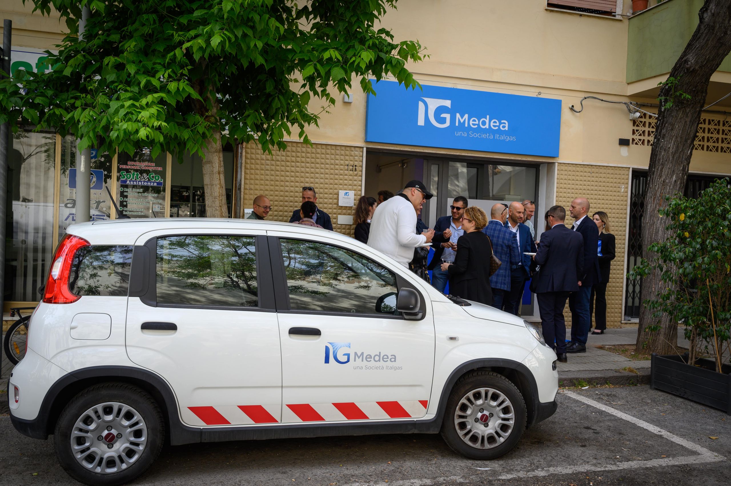 Un'auto aziendale Medea Italgas parcheggiata all'esterno di un infopoint con persone che conversano.