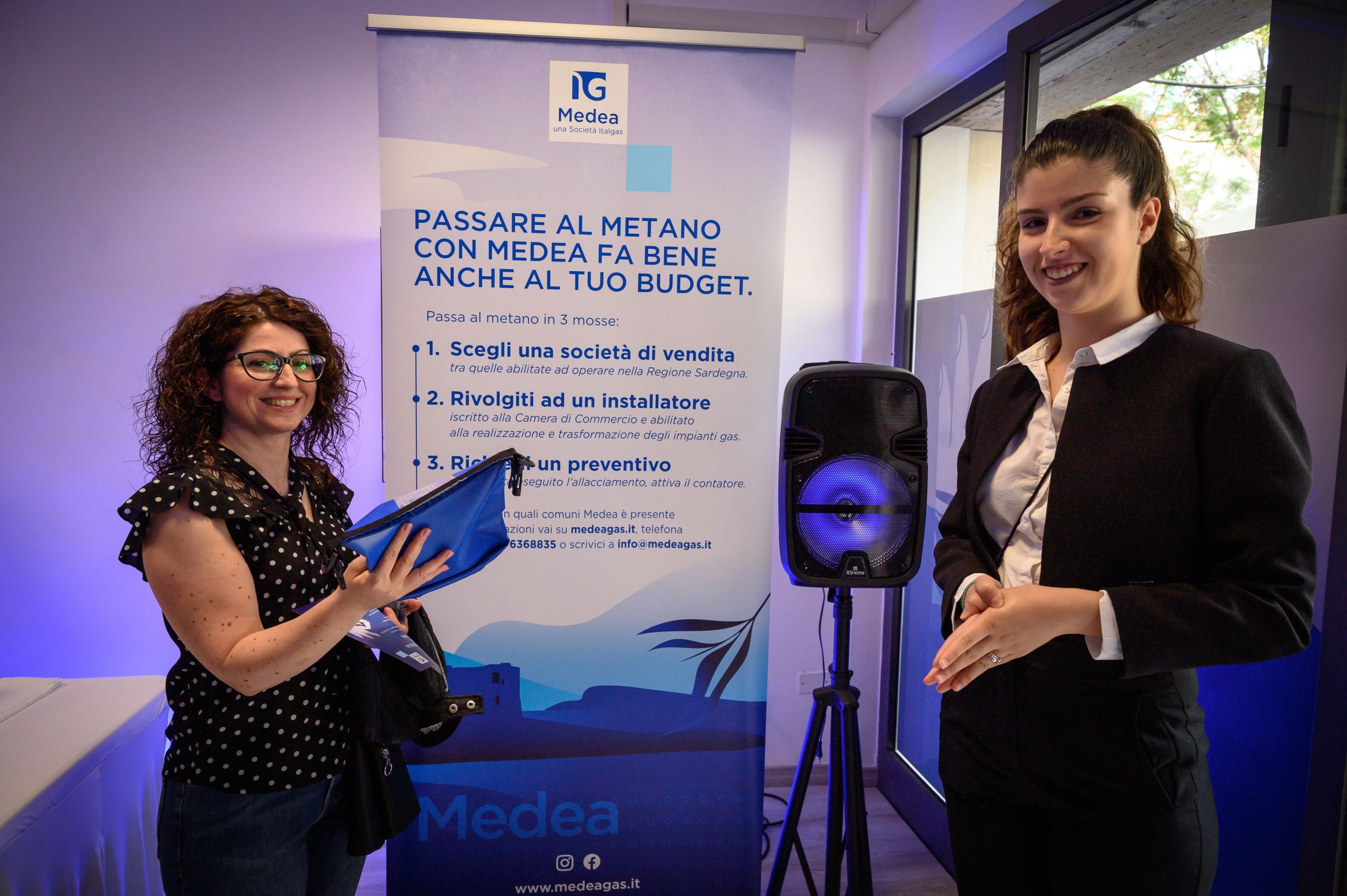 Due persone sorridono in un infopoint Medea Italgas con materiali promozionali.