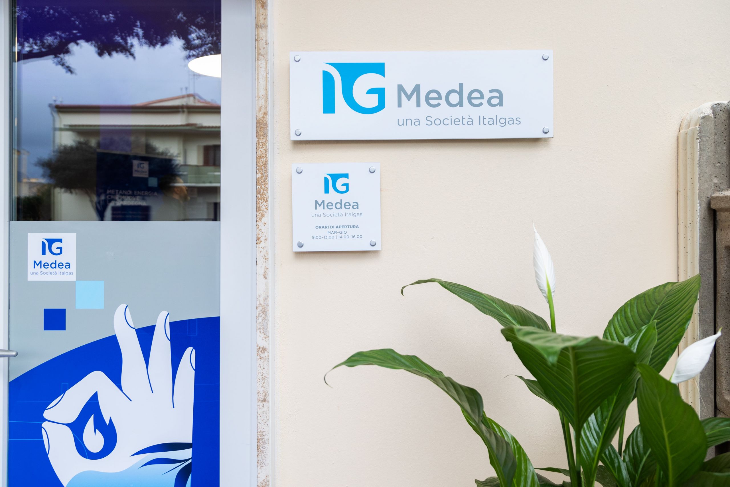 Insegna "Medea una Società Italgas" su parete esterna, con orari di apertura e logo aziendale.