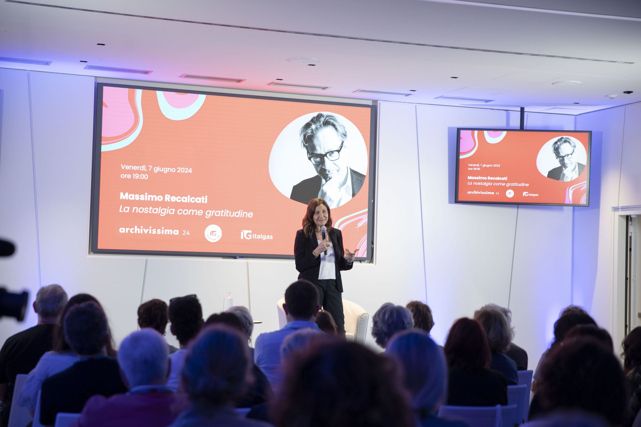 Relatrice parla all'Heritage lab evento con slide di Massimo Recalcati su 'La nostalgia come gratitudine' sullo sfondo.