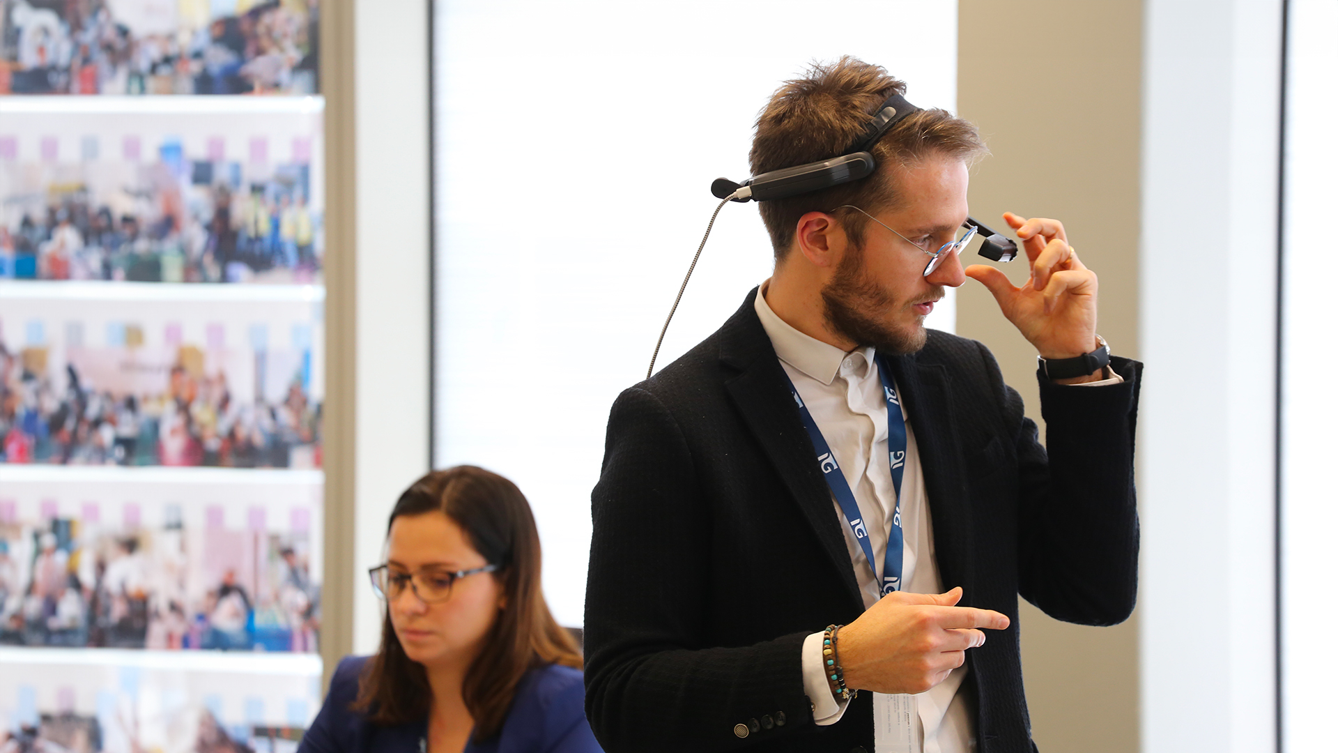 Man with technological device on forehead and woman on background working in office