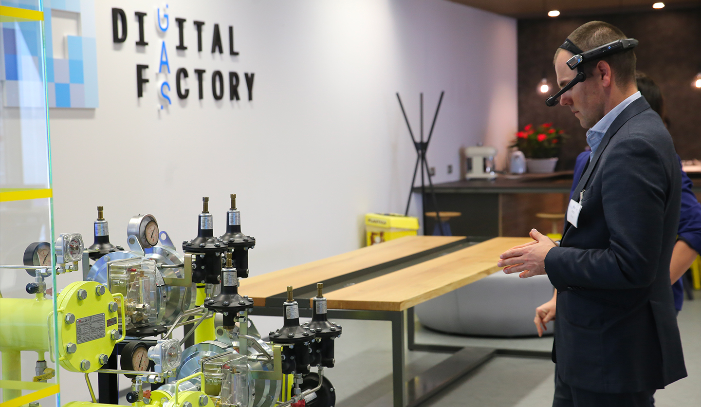 Uomo in abiti formali usa visore AR in laboratorio Italgas per innovazione sostenibile.