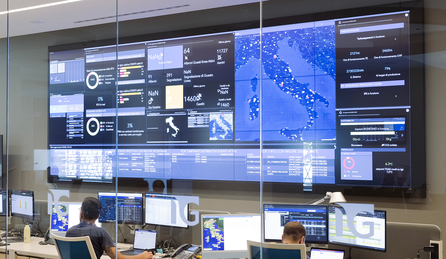 Italgas control room with people at the PC, large monitors showing data for energy efficiency and emissions reduction.
