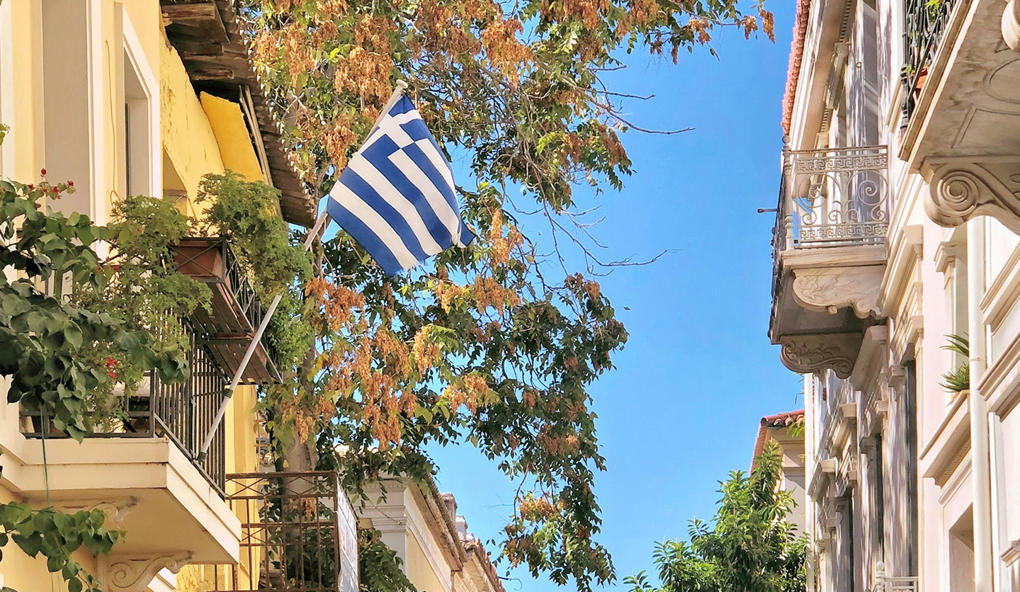 Greek road with flag and trees, symbolizes Italgas' commitment to biodiversity and local communities.