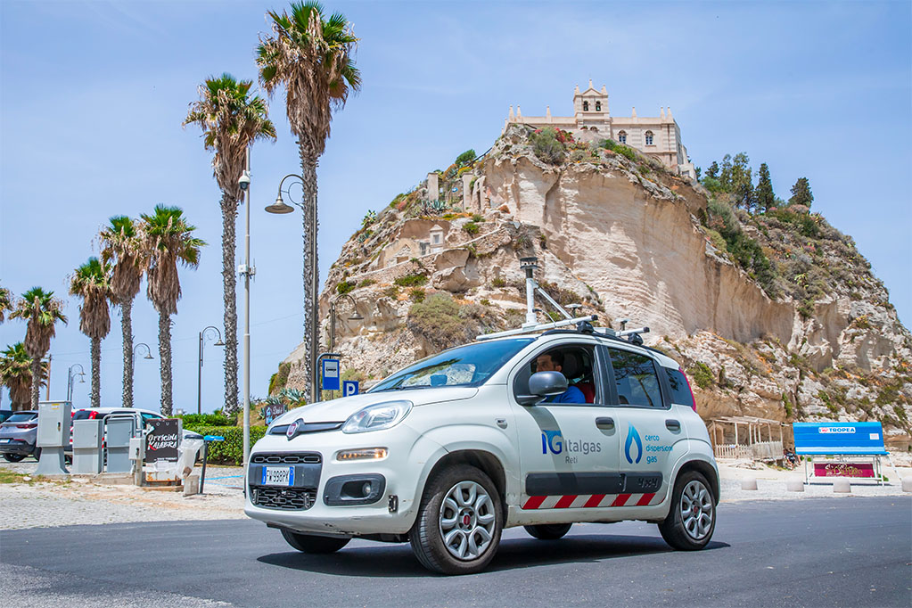 Auto Italgas Picarro parcheggiata, con uno sfondo di palme e una scogliera con un edificio in cima e il cielo azzurro.